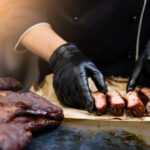 Grill restaurant kitchen. Cropped shot of chef in black cooking gloves serving smoked pork ribs.